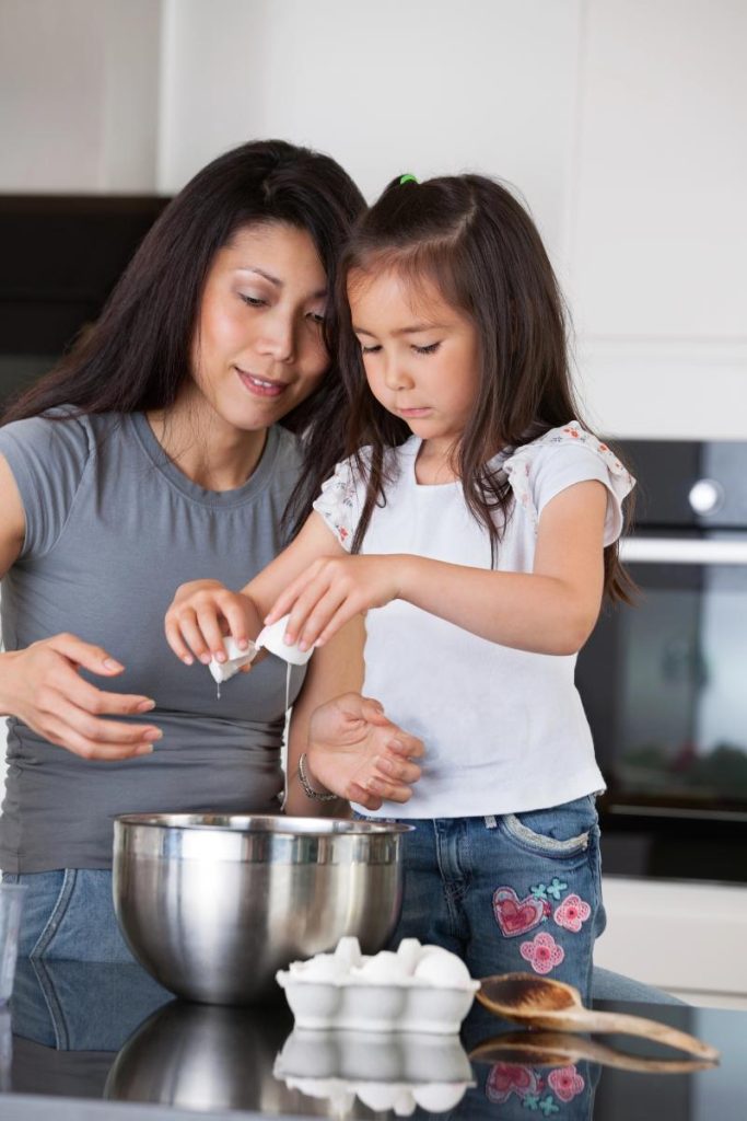 mom and daughter cracking eggs into a bowl