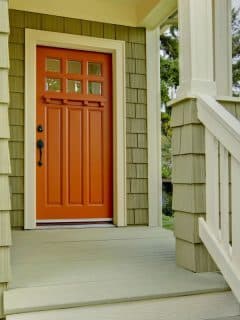 orange door on green house with front porch