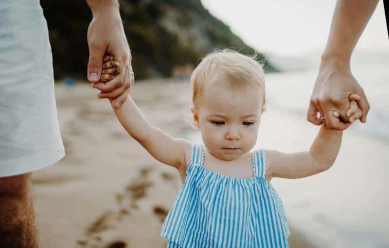 father and mother holding baby girl's hand on beach