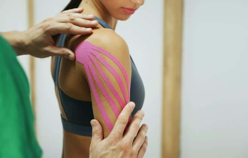pink tape applied to woman's shoulder for physical therapy