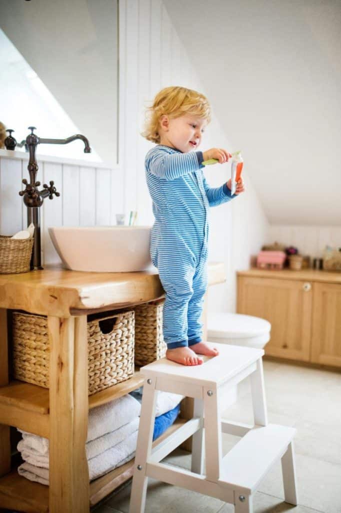 toddler boy in striped pajamas putting toothpaste on toothbrush