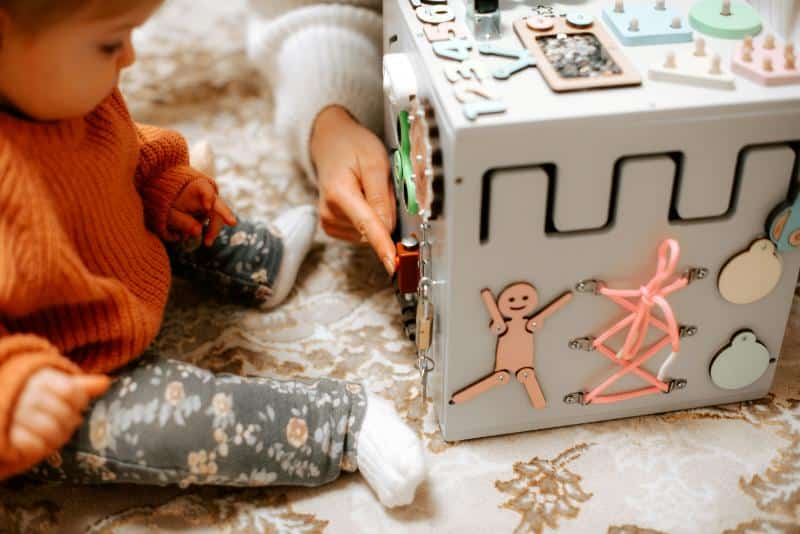 baby with toy cube with lots of interactive elements with parent demonstrating how to use it