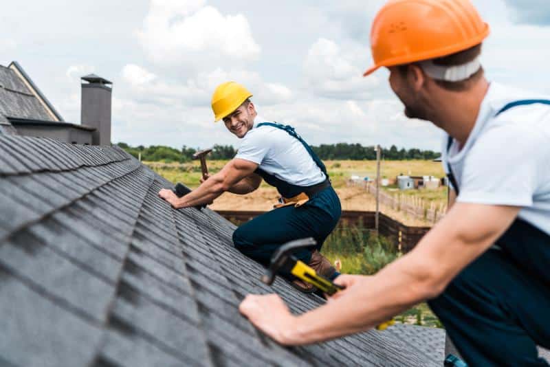 two men in hard hats working on a shingled roof