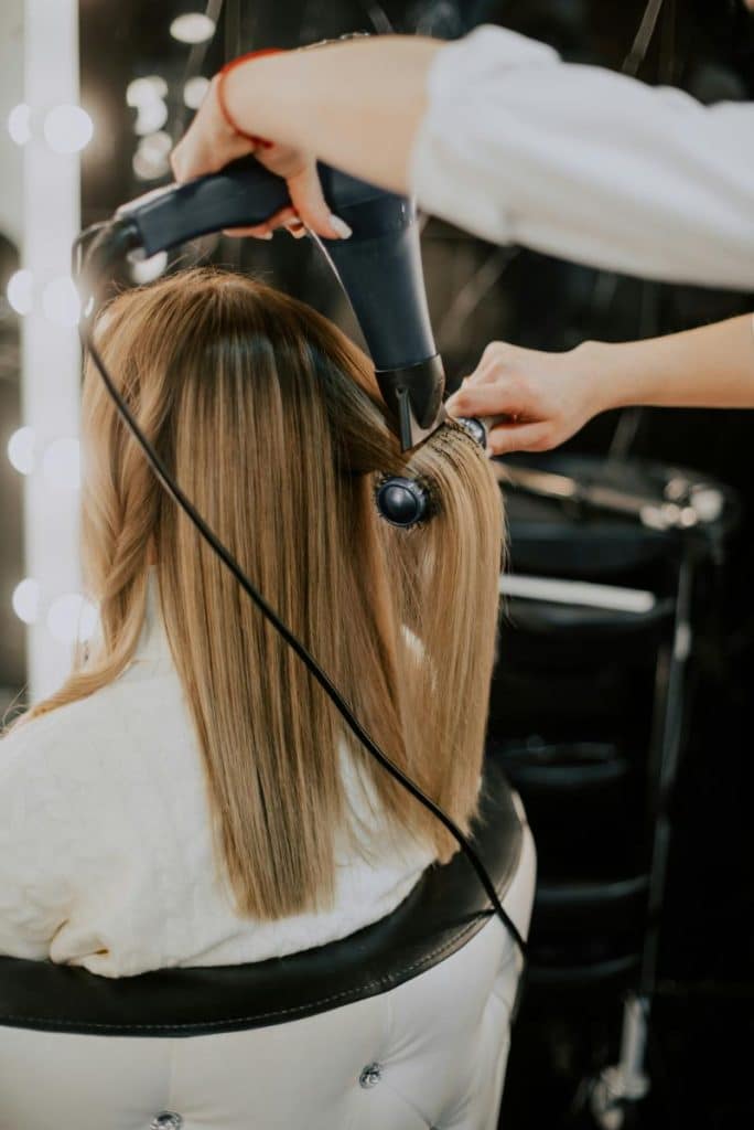 woman getting hair blow dried and curled by stylist