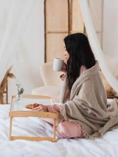 side view of woman having coffee and a croissant in bed