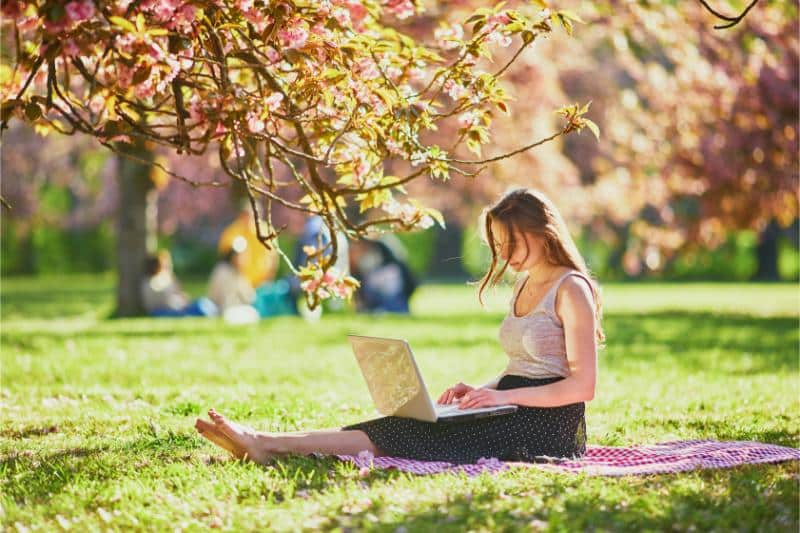 woman sitting in park with laptop during cherry blossom season in France