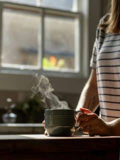 woman standing at kitchen counter with steaming cup of coffee