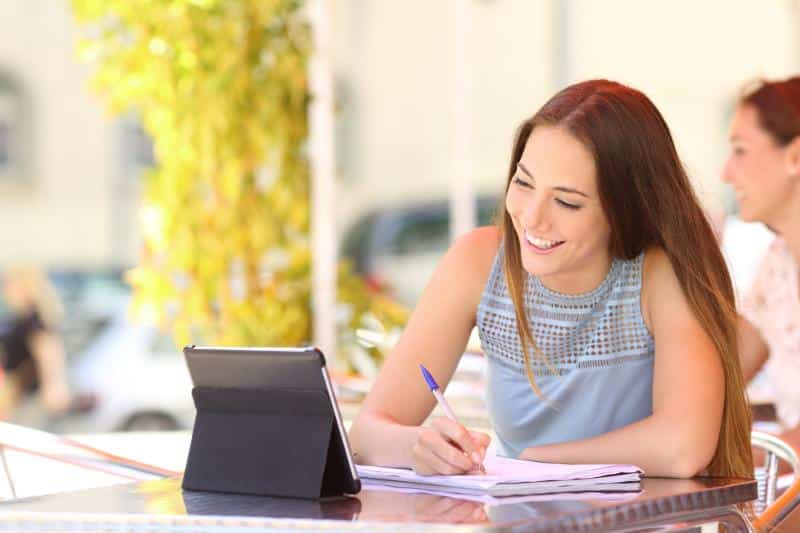 woman watching tablet while taking notes