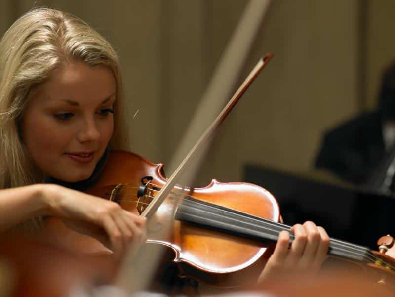 blonde woman drawing bow over the strings of a violin