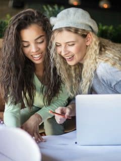 women smiling while looking at papers with laptop off to the side