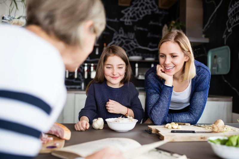 grandmother looking at cookbook while daughter and granddaughter look on