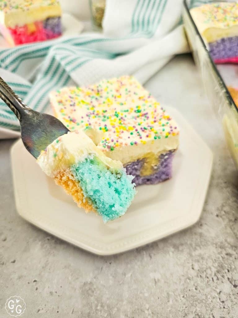 rainbow poke cake with fork in foreground