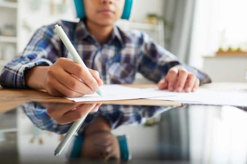 boy using a tablet and writing on paper at a table