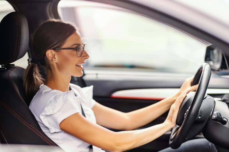 brunette woman with glasses with hands on steering wheel in car