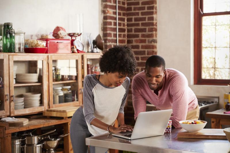 black couple looking at something on laptop while standing in the kitchen