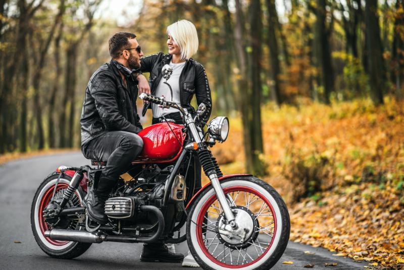 couple with red motorcycle - man sitting on motorcycle while blonde woman stands beside it