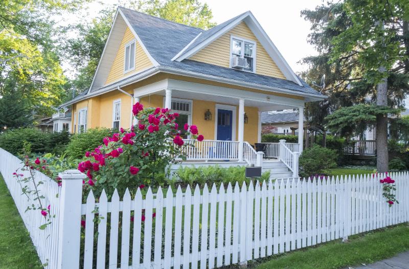 yellow house with blue front door surrounded by white picket fence