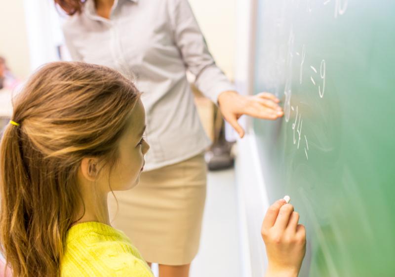 elementary girl doing math problem on chalkboard