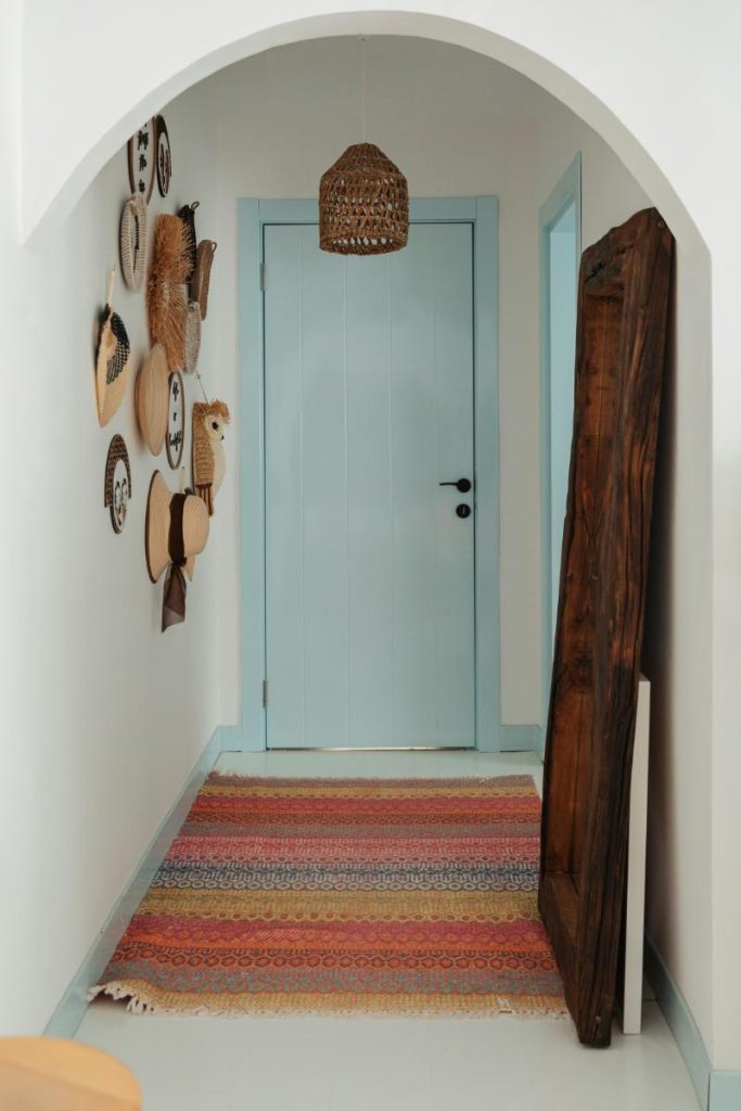 entryway with light blue door, colorful rug, and a fun display of decor on the left wall