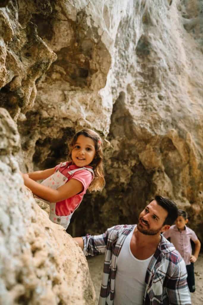 girl climbing on rocks while father watches