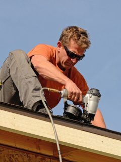 guy on edge of roof installing shingles