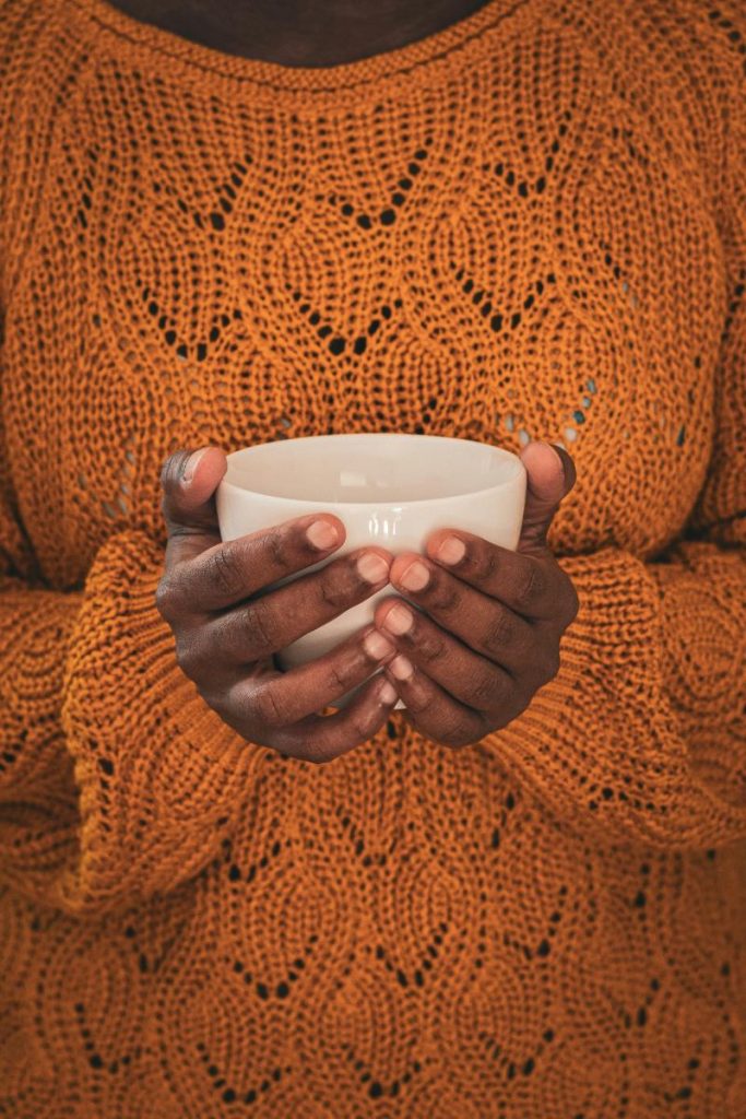 black woman in orange sweater holding a cup of tea