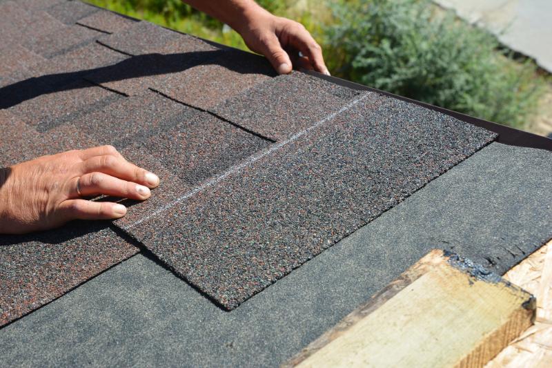 man's hands installing asphalt shingles on roof