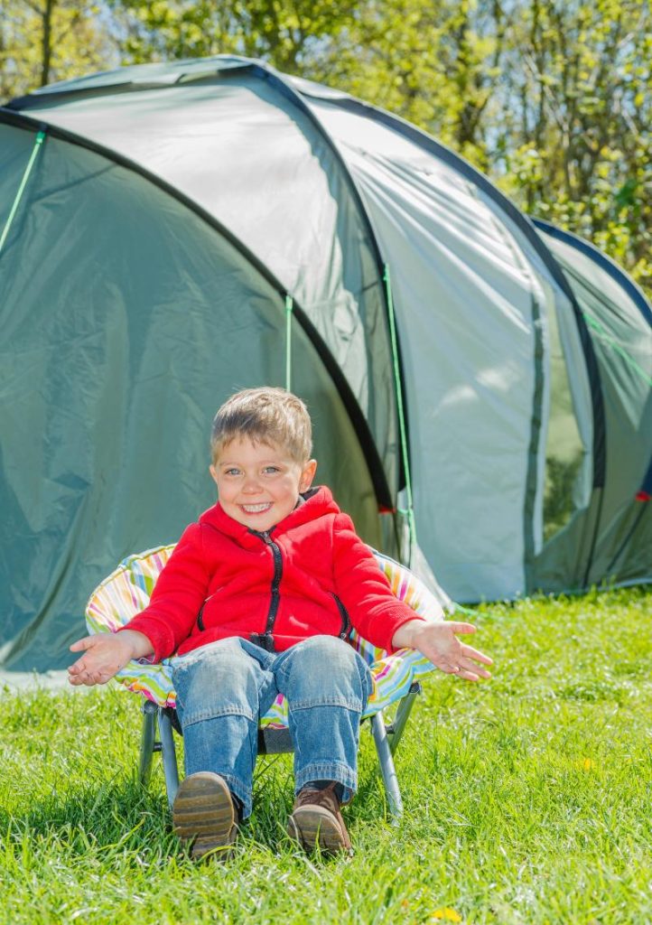 little boy sitting in chair in front of tent