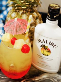 layered malibu sunset cocktail garnished with pineapple and cherry