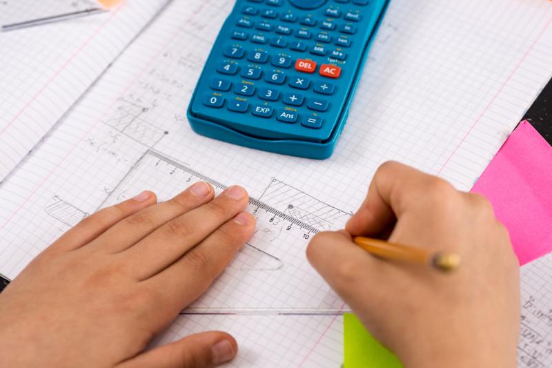 boy using graphic paper, a calculator, and a  protractor to solve a math problem