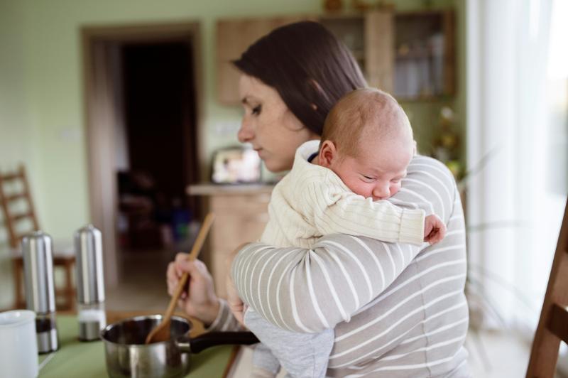 mom holding baby while stirring food in pot