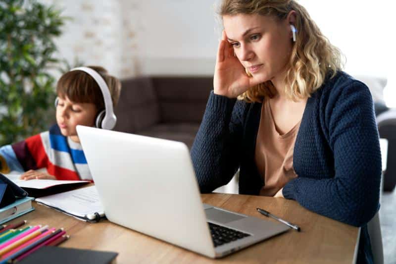 mom using laptop and earbuds with her son sitting beside her