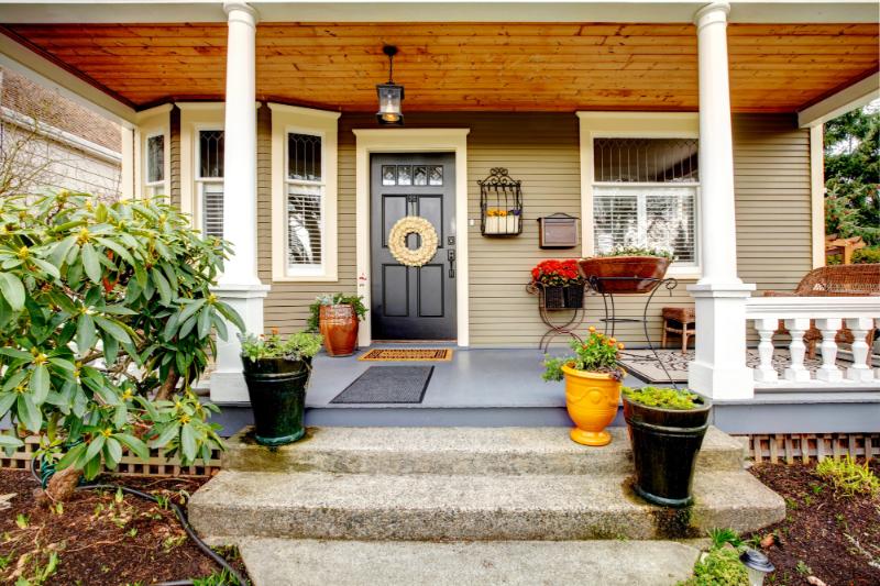 house with black door and cute wreath, porch has several potted plants and flowers