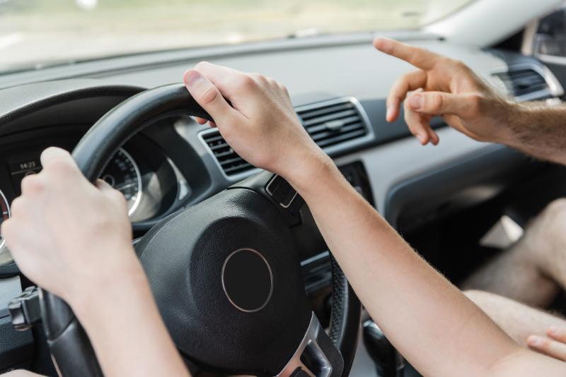 teen's hands on the steering wheel, father pointing from passenger seat