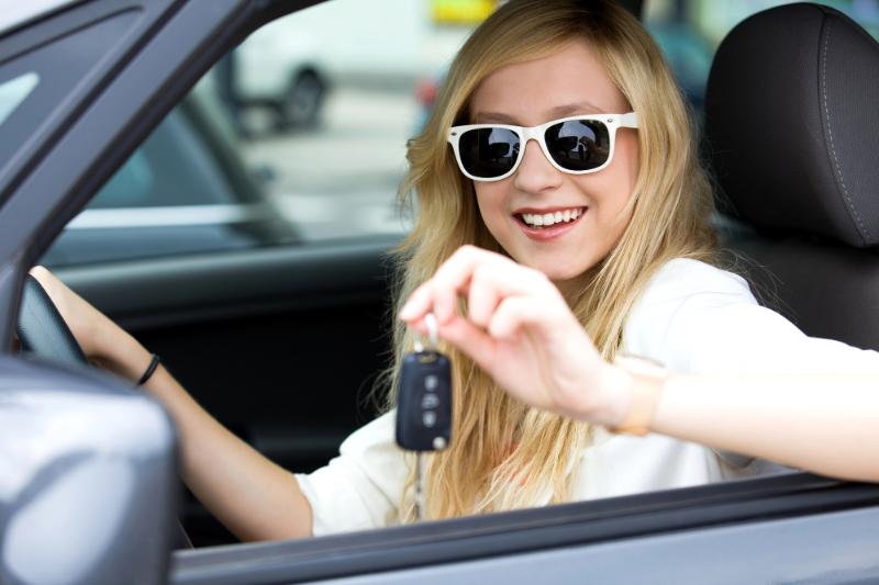 blonde teen girl wearing sunglasses in car, holding car key fob in her hand