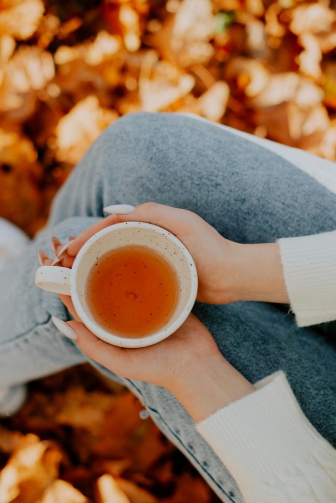 woman's hands holding a cup of tea - autumn leaves in background