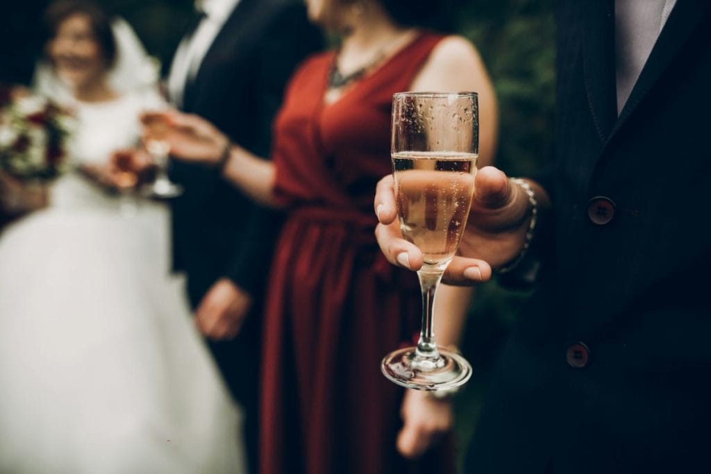 champagne glass in hand with wedding guest and bride and groom in background