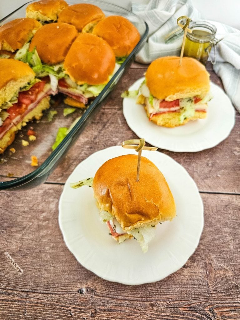 Italian sub sliders on plates with rest of sandwiches in tray