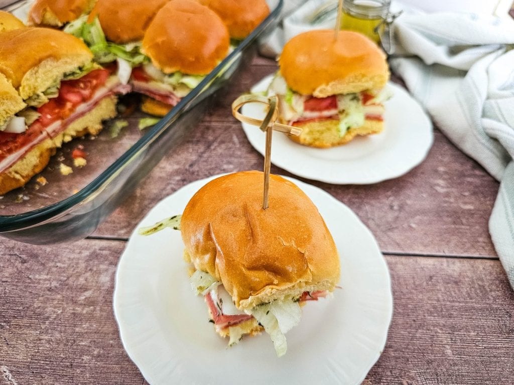 cold Italian sub sliders on white plates with the rest in a dish in the background