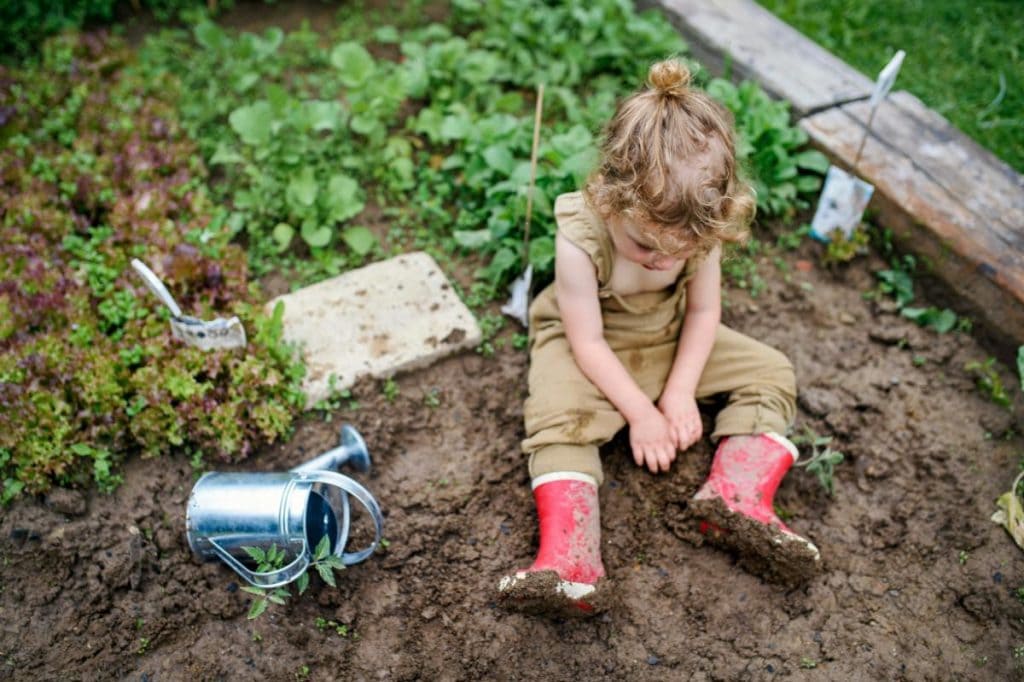little girl in overalls and rainboots sitting in the mud