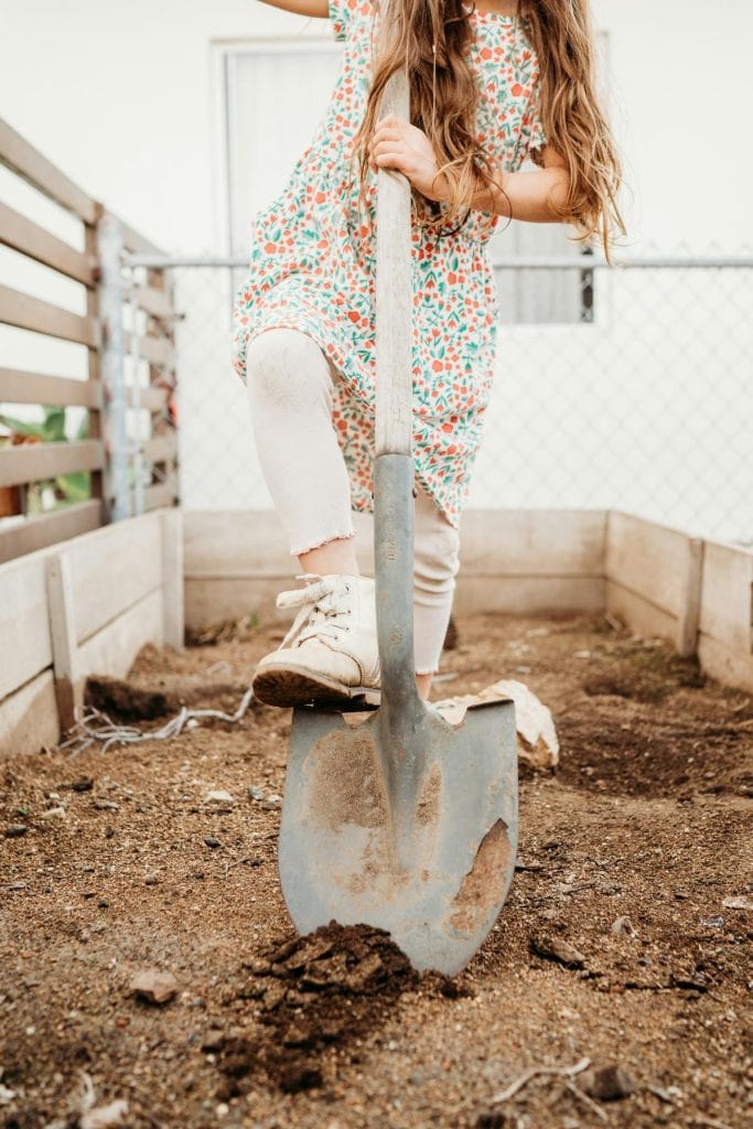 girl using a shovel in a flower bed