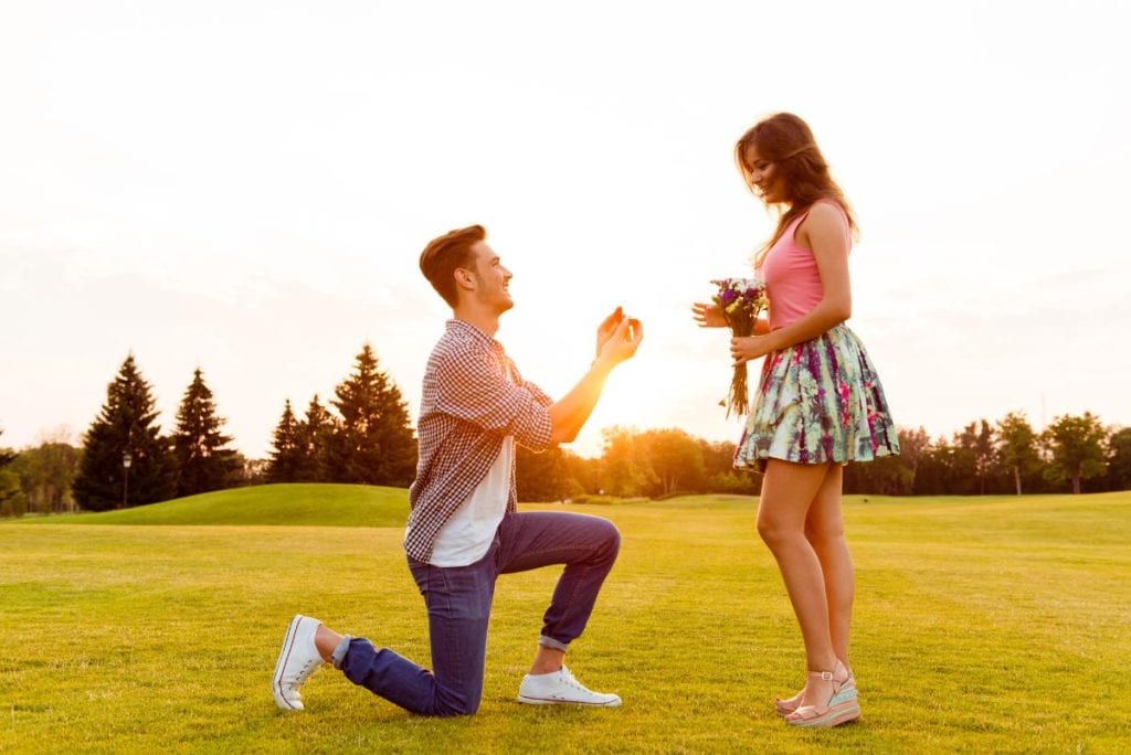 guy in grassy field proposing to girlfriend
