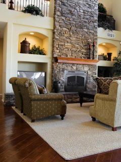 living room with hardwood floors, large cream rug, and stone fireplace