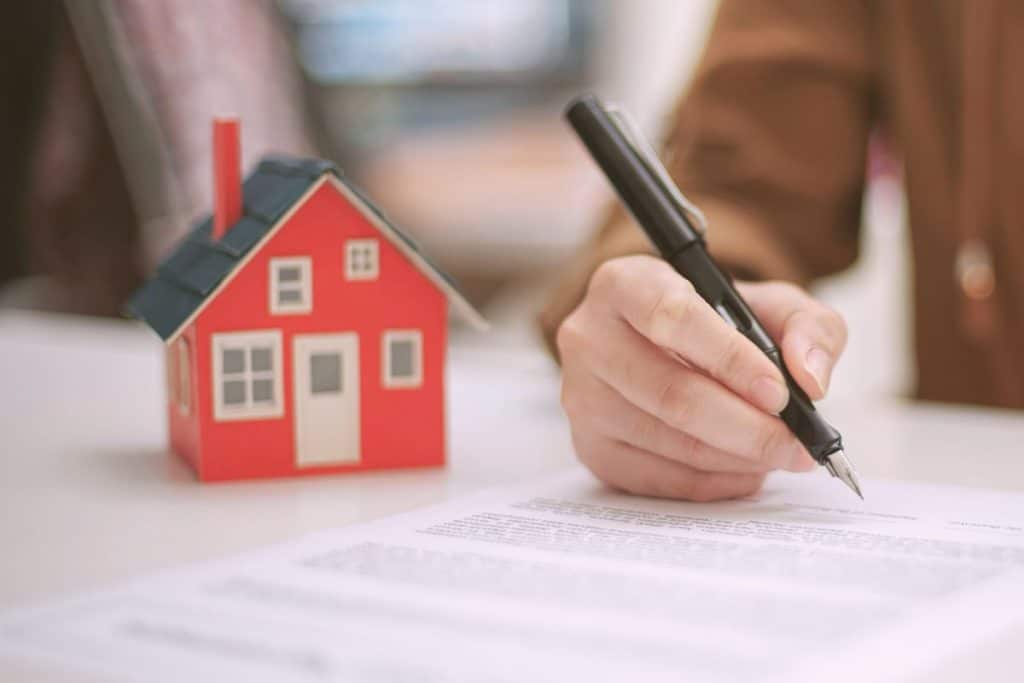 man signing a contract with model of red house beside his hand
