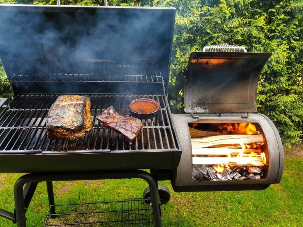 bbq smoker with meat on the grill and wood fire on the side