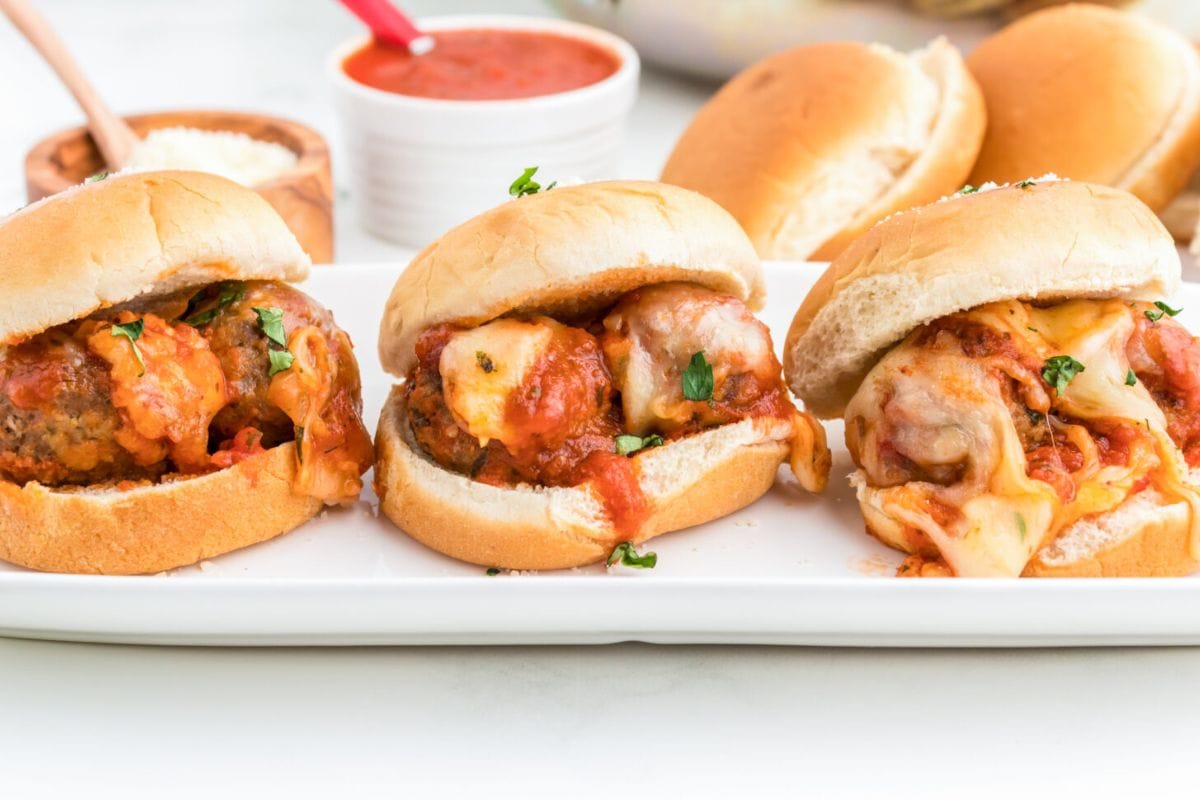 three meatball sliders on white plate with more in background