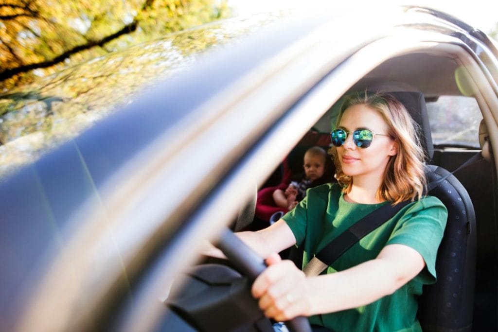 mom with sunglasses driving car, baby in backseat in car seat