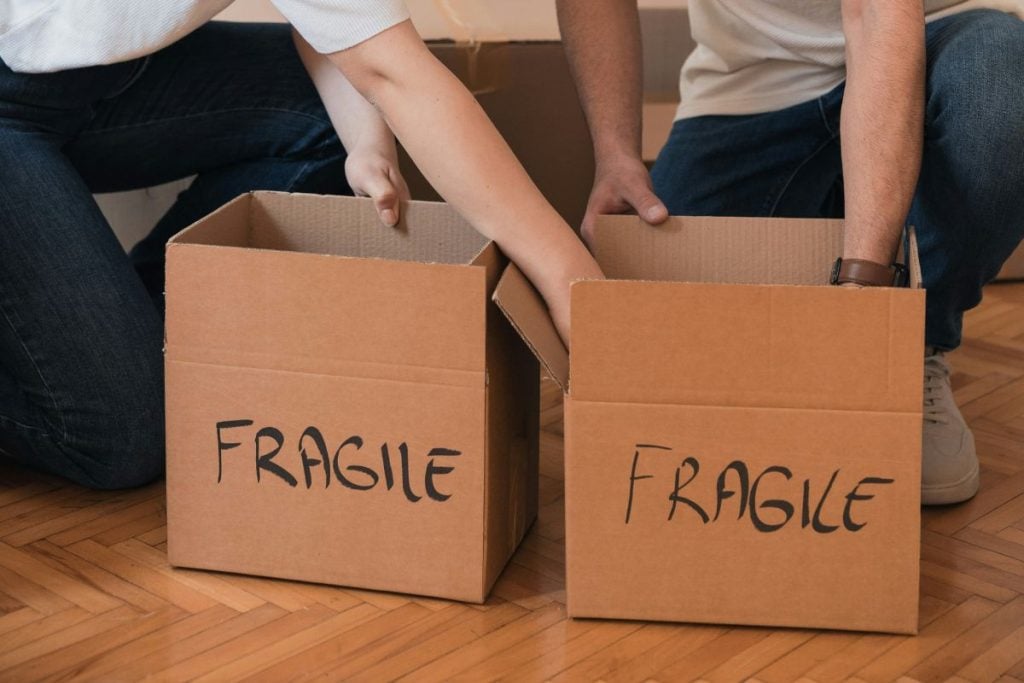 man and woman with hands reaching into boxes labeled 'fragile'