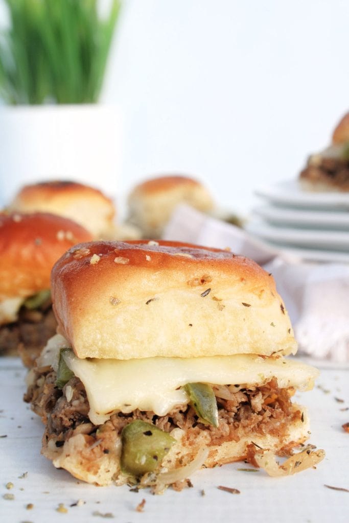 vertical image of philly cheesesteak sliders with one in front and several in the background