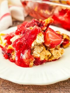 close-up of strawberry cheesecake dump cake on white plate with baking dish behind